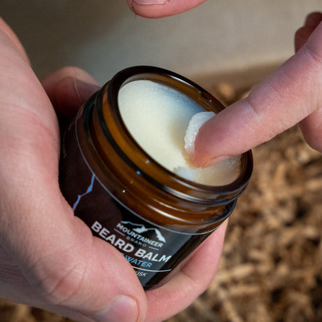 Mountaineer Brand Products beard balm color and consistency shown in a jar with a hand holding it.