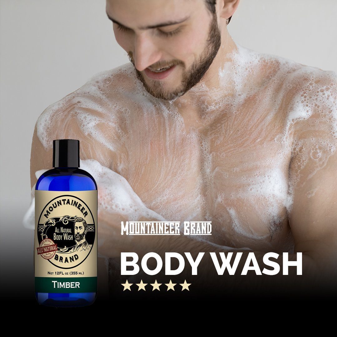 A man with a beard smiling while covered in suds, standing next to a bottle of Mountaineer Brand Products Natural Men's Body Wash with a five-star rating.