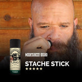 A man with a beard is holding a Mountaineer Brand Products Mustache Wax - 9 Scents Available.
